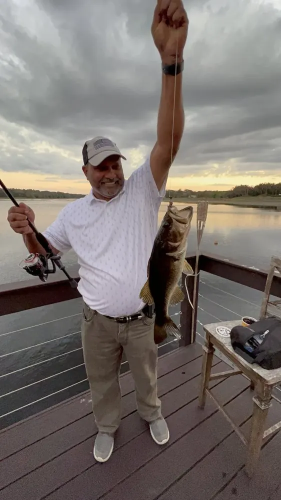 Kris Persaud holding up a fish on a lake dock at sunset